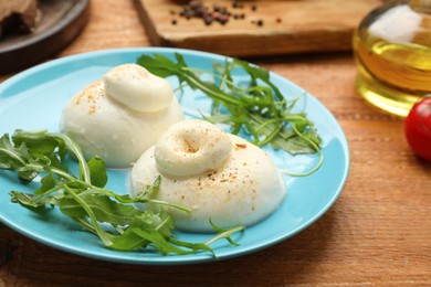 Photo of Delicious burrata cheese with arugula on wooden table, closeup