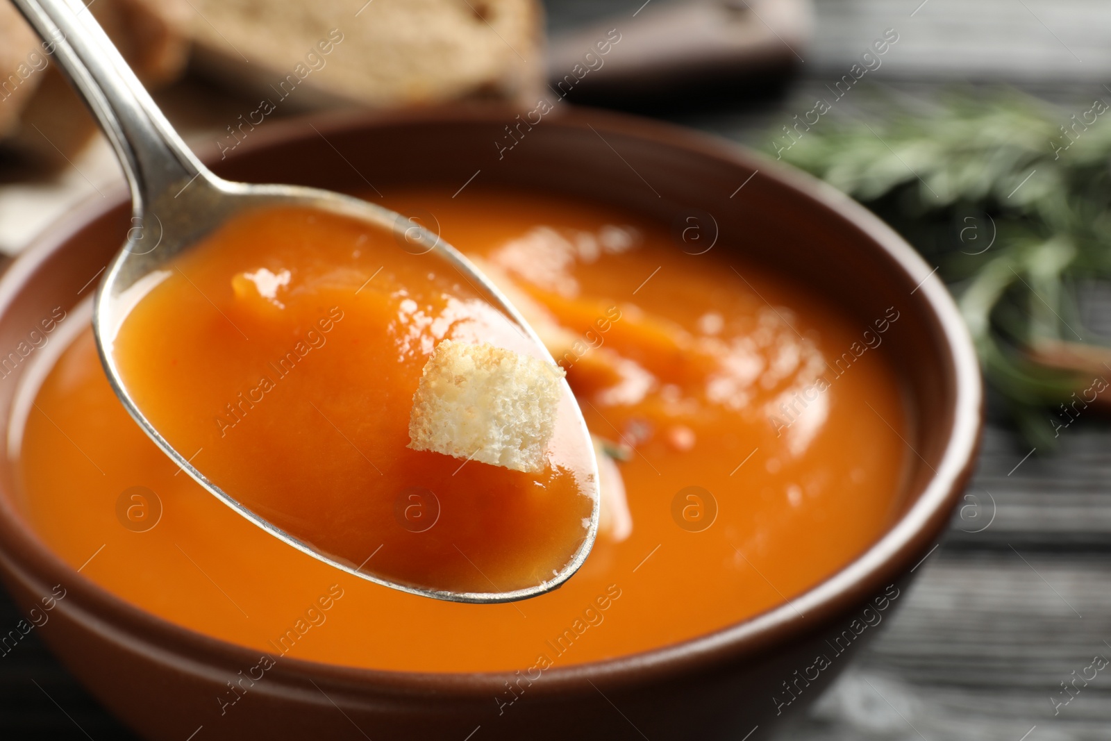 Photo of Spoon of sweet potato soup with crouton over bowl, closeup