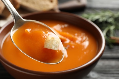 Spoon of sweet potato soup with crouton over bowl, closeup