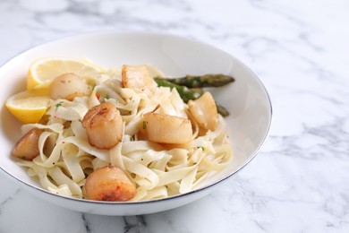 Photo of Delicious scallop pasta with asparagus and lemon on white marble table, closeup