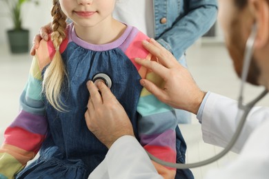 Photo of Mother and daughter having appointment with doctor. Pediatrician examining patient with stethoscope indoors, closeup