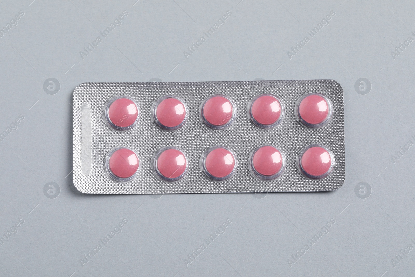 Photo of Pink pills in blister on grey background, top view