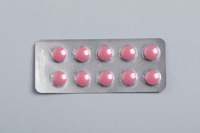 Photo of Pink pills in blister on grey background, top view