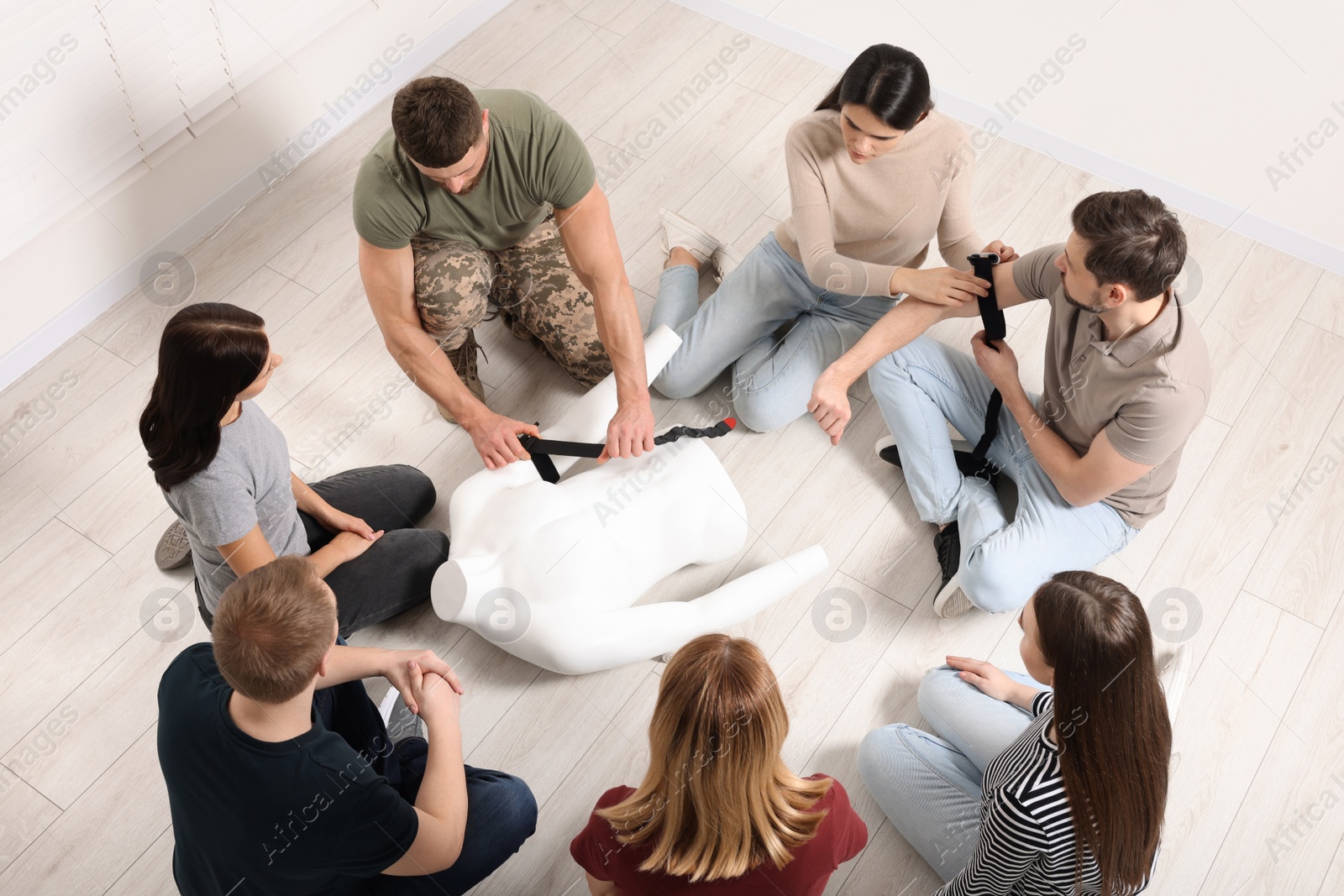 Photo of Soldier in military uniform teaching group of people how to apply medical tourniquet indoors, above view