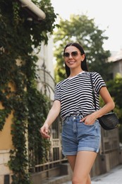 Beautiful young woman in stylish sunglasses walking on city street