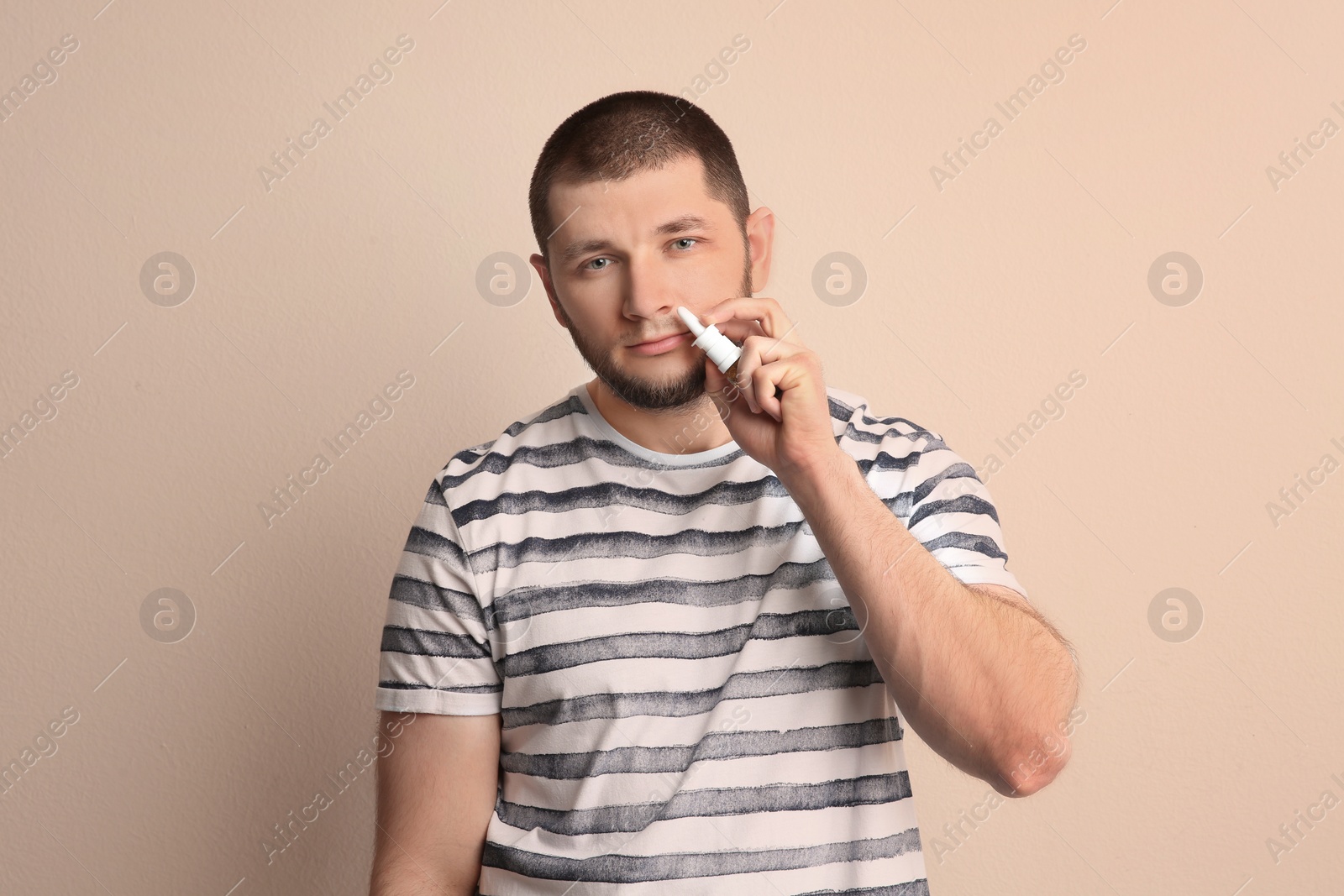 Photo of Sick man using nasal spray on light background