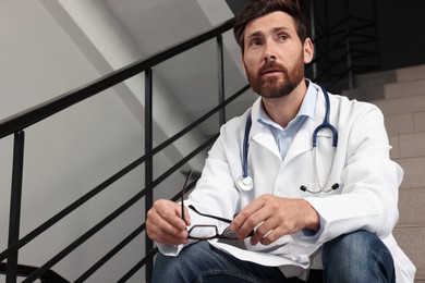 Photo of Doctor with glasses sitting on stairs in hospital