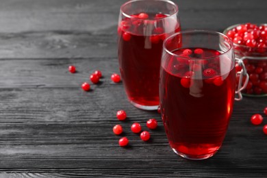Photo of Tasty cranberry juice in glasses and fresh berries on black wooden table, closeup. Space for text