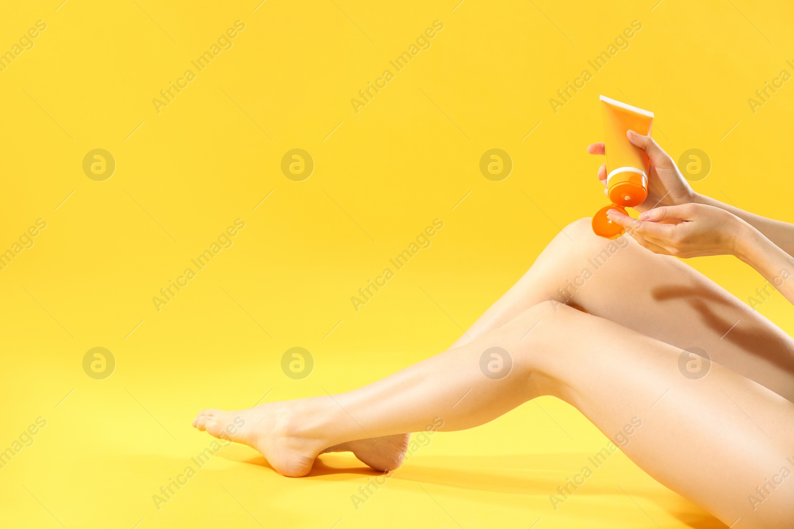 Photo of Woman applying sun protection cream on leg against yellow background, closeup. Space for text