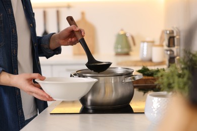 Woman pouring tasty soup into bowl at countertop in kitchen, closeup