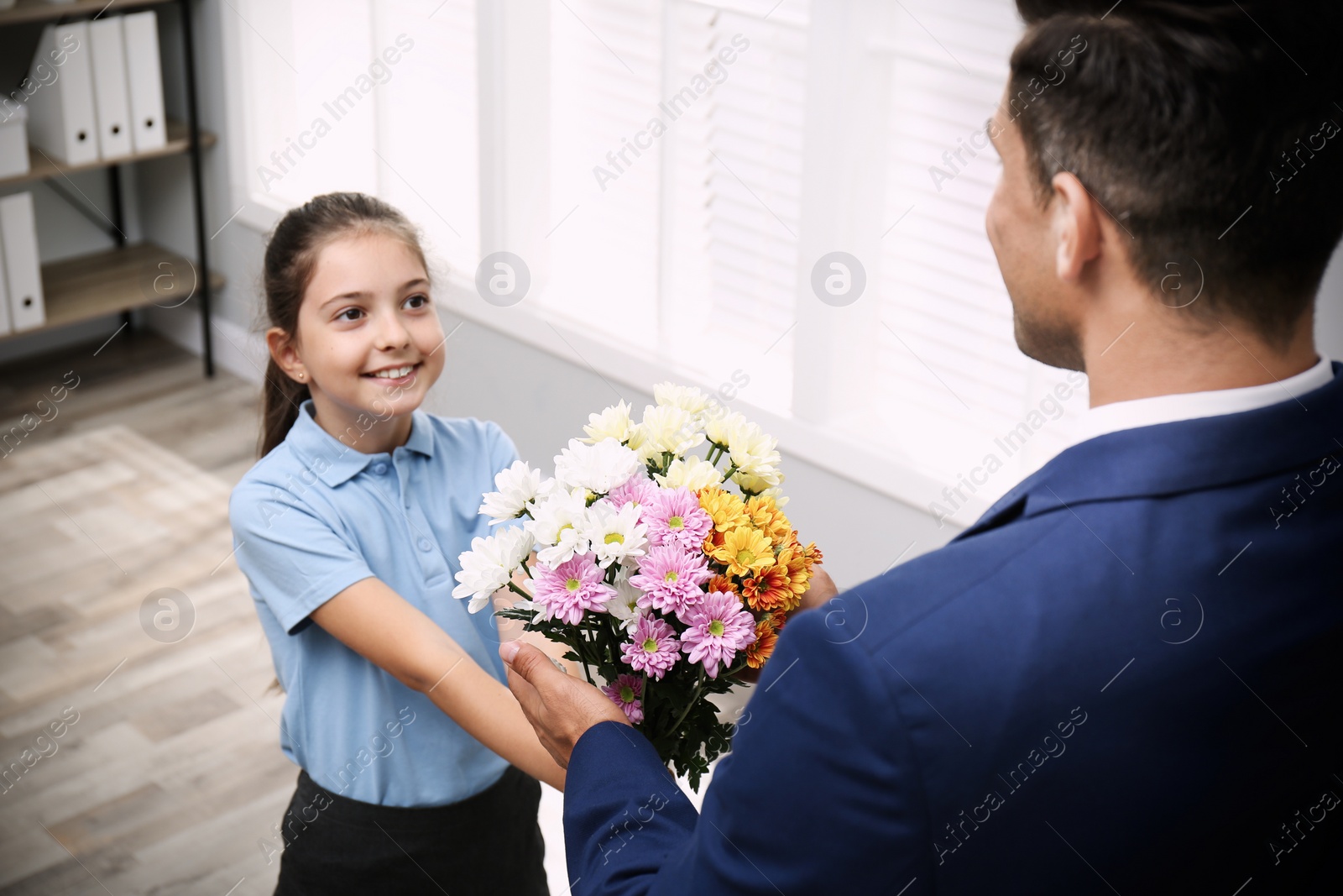 Photo of Schoolgirl congratulating her pedagogue with bouquet in classroom. Teacher's day