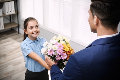 Photo of Schoolgirl congratulating her pedagogue with bouquet in classroom. Teacher's day