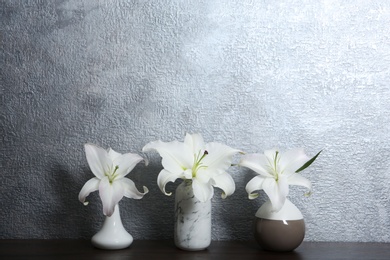 Photo of Vases with beautiful flowers on table against color background