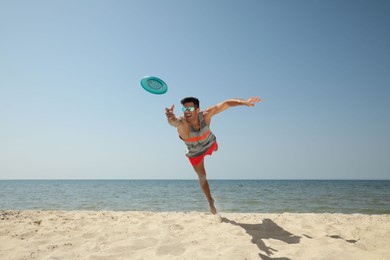 Photo of Sportive man jumping while trying to catch flying disk at beach