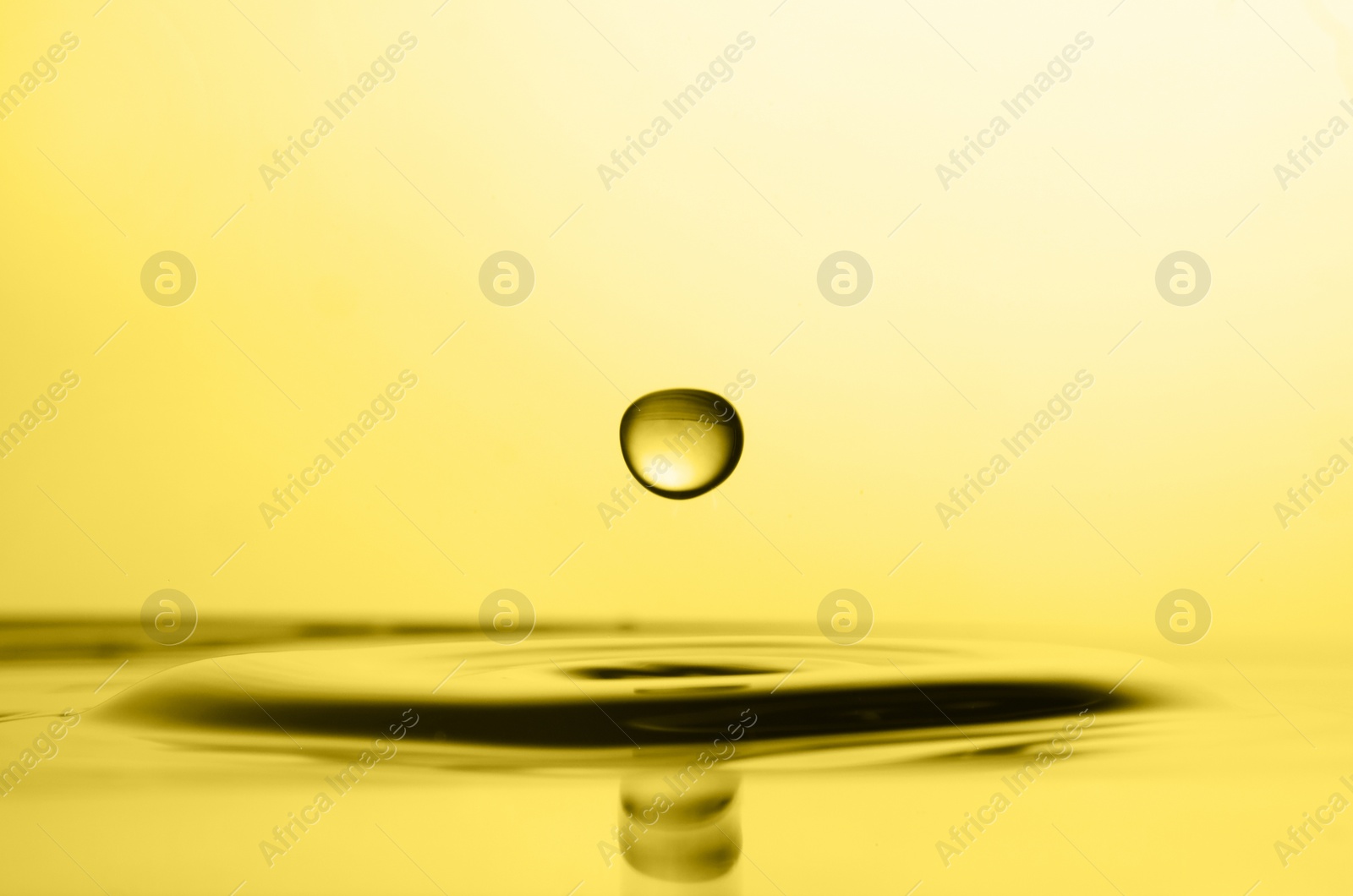 Image of Splash of golden oily liquid with drop on yellow background, closeup