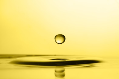 Image of Splash of golden oily liquid with drop on yellow background, closeup