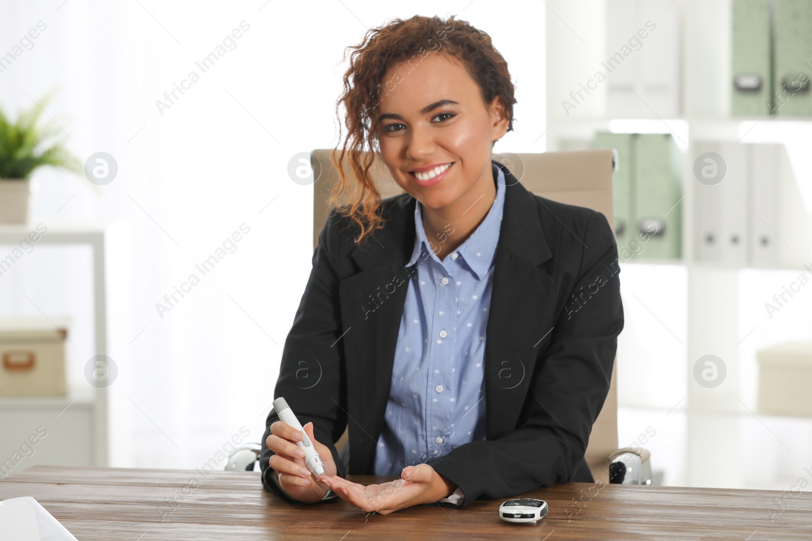 Photo of Young African-American woman using lancet pen at workplace. Diabetes control