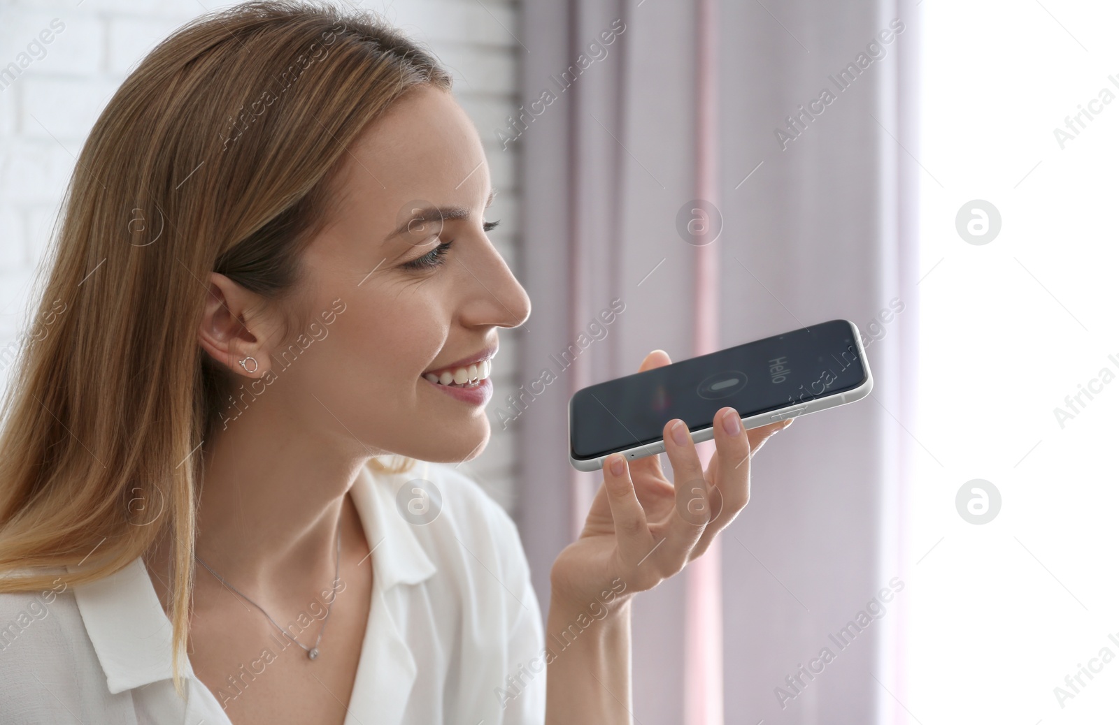 Photo of Young woman using voice search on smartphone indoors