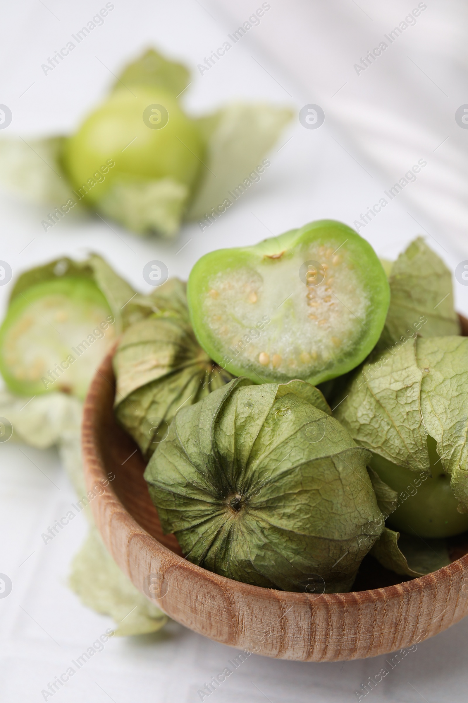 Photo of Fresh green tomatillos with husk in bowl on light table, closeup