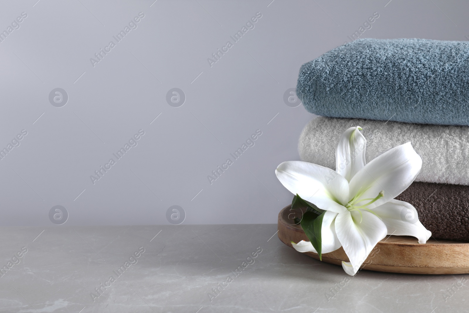 Photo of Stack of clean bath towels and beautiful flower  on grey table. Space for text