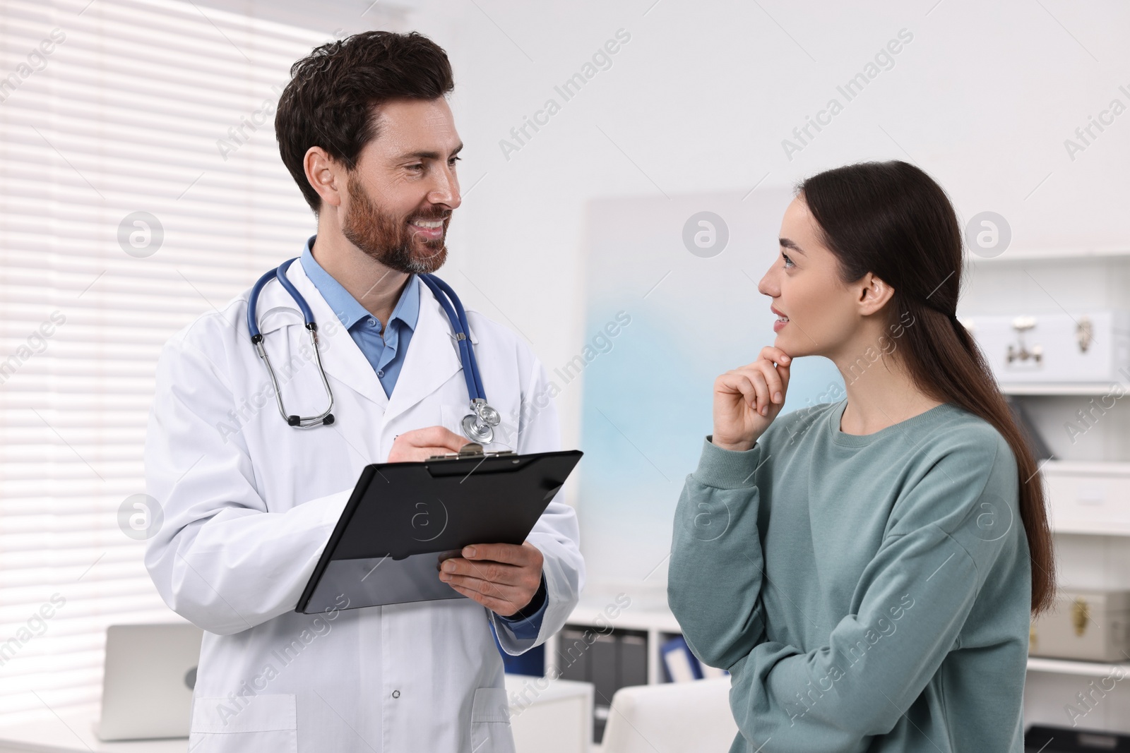 Photo of Doctor with clipboard consulting patient during appointment in clinic