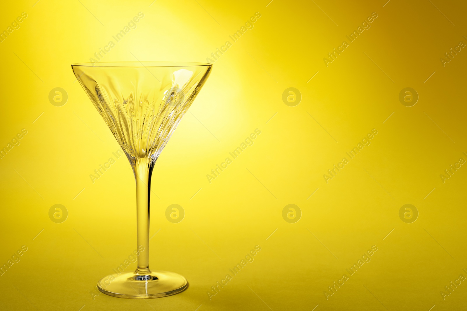 Photo of Elegant empty martini glass on yellow background. Space for text