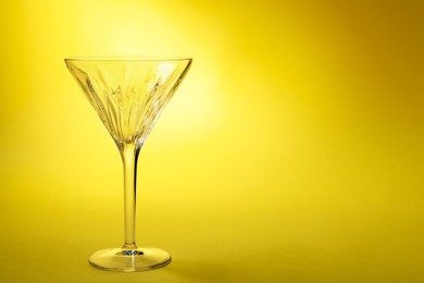 Photo of Elegant empty martini glass on yellow background. Space for text