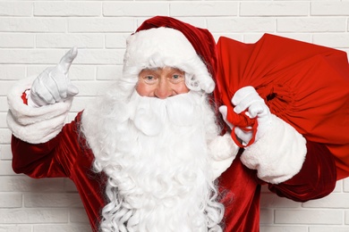 Authentic Santa Claus with bag full of gifts against white brick wall