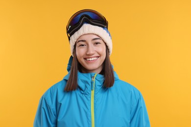 Photo of Winter sports. Happy woman with snowboard goggles on orange background