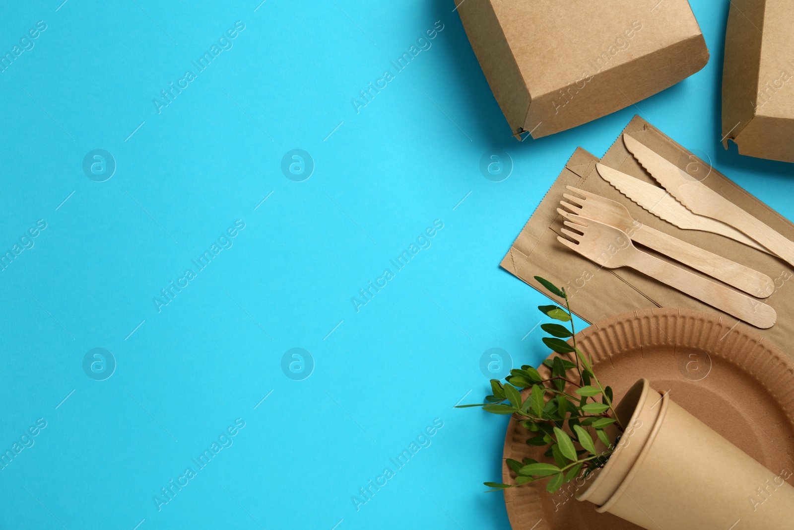 Photo of Flat lay of paper and wooden tableware with green twigs on turquoise background, space for text. Eco friendly lifestyle