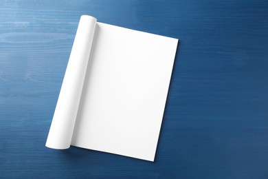 Photo of Open magazine with blank page on blue wooden table, top view. Space for text