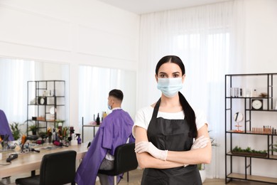 Professional stylist with protective mask in salon, space for text. Hairdressing services during Coronavirus quarantine