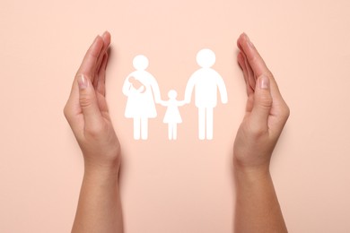 Image of Woman holding hands around paper silhouette of family on pink background, top view. Insurance concept