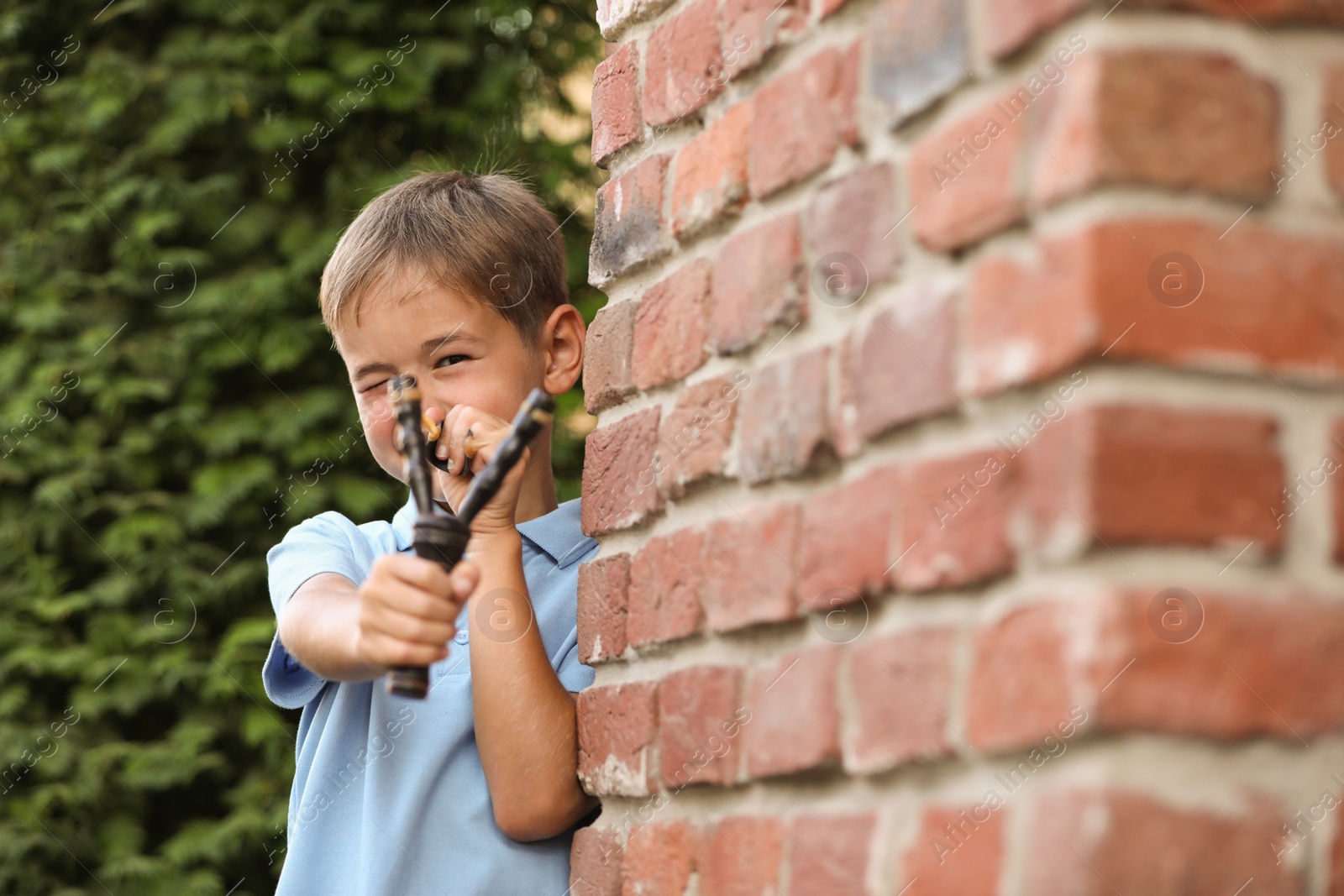 Photo of Little boy playing with slingshot outdoors. Space for text