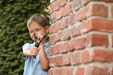 Photo of Little boy playing with slingshot outdoors. Space for text