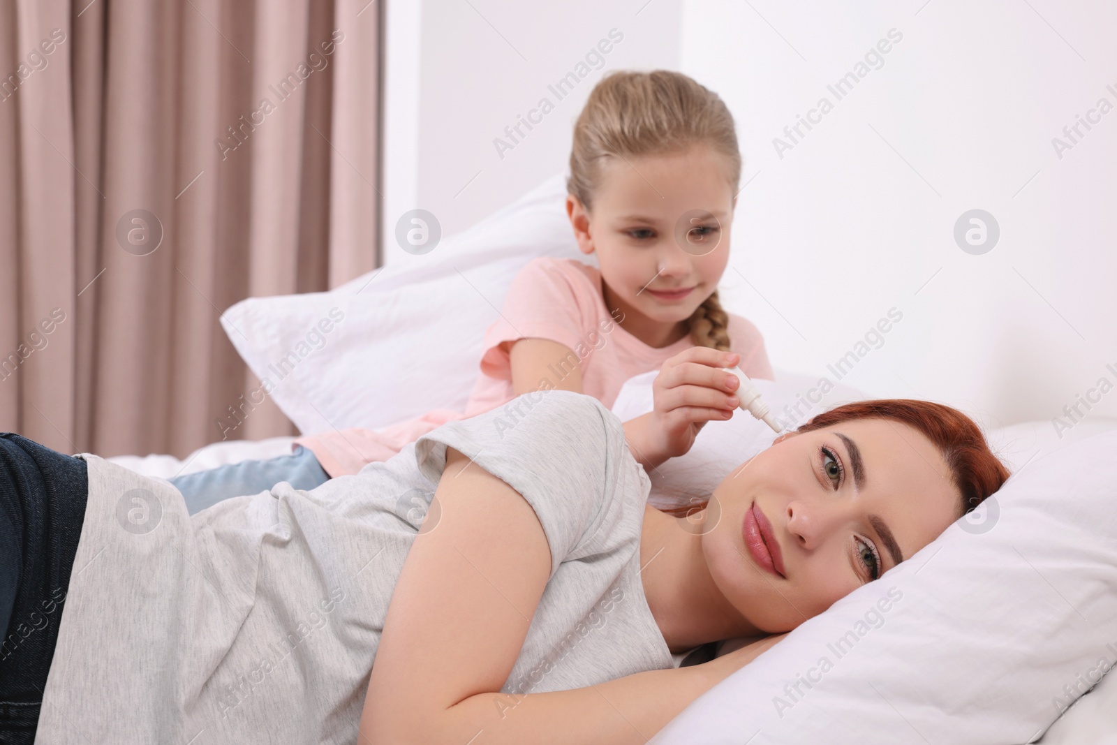 Photo of Little girl dripping medication into mother's ear in bedroom