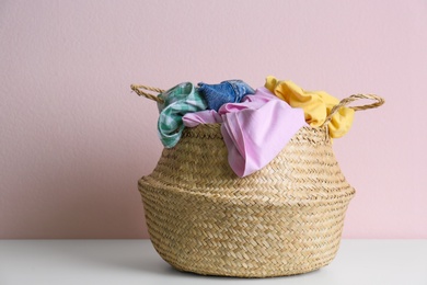Photo of Wicker laundry basket with different clothes on grey table near pink wall