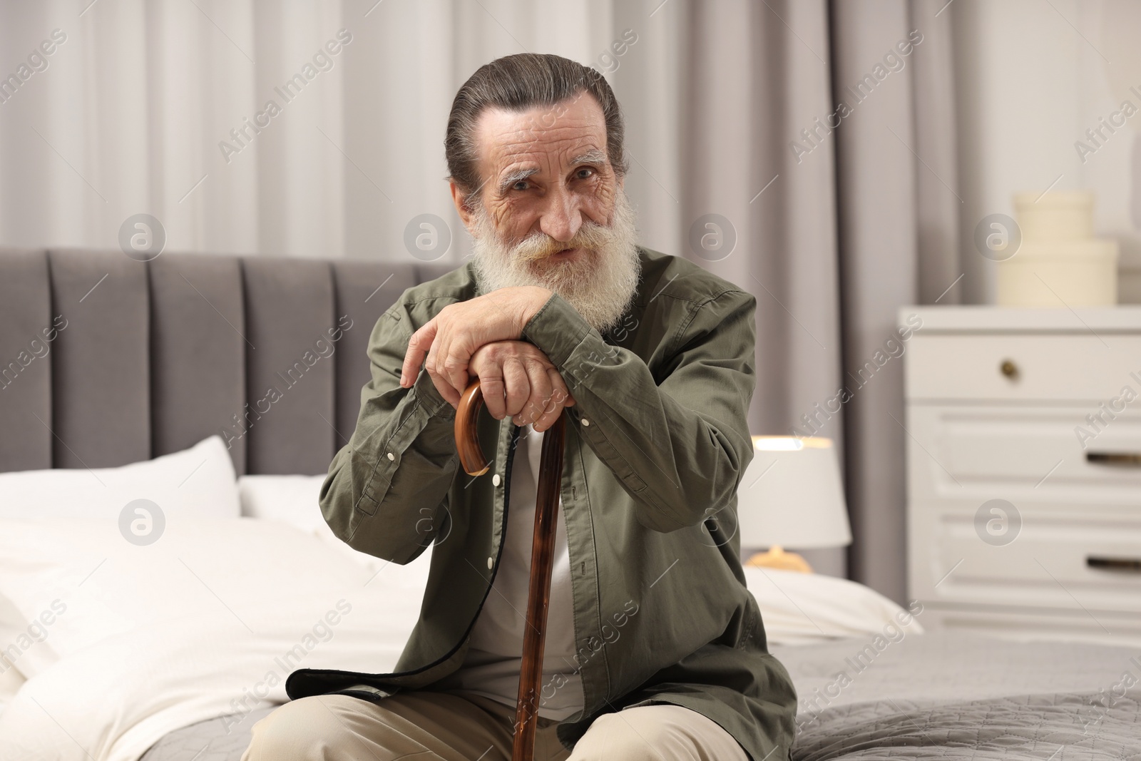 Photo of Senior man with walking cane on bed at home