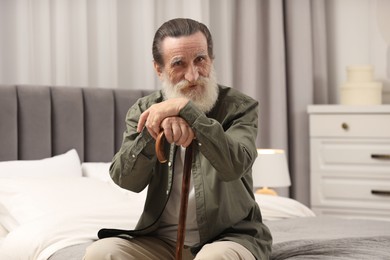 Photo of Senior man with walking cane on bed at home