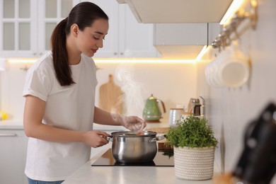 Beautiful woman cooking soup in light kitchen