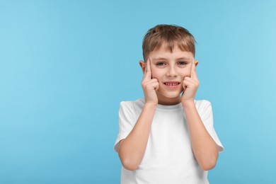 Little boy suffering from headache on light blue background, space for text