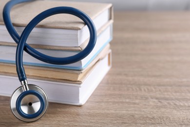 Photo of Stack of student textbooks and stethoscope on wooden table, closeup view with space for text. Medical education