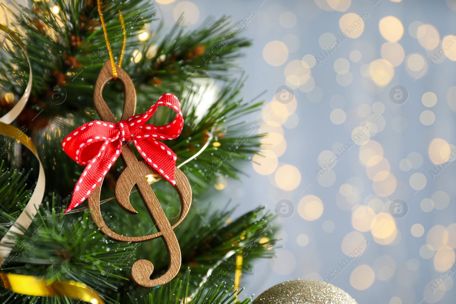 Photo of Wooden music note with red bow hanging on Christmas tree against blurred lights. Space for text