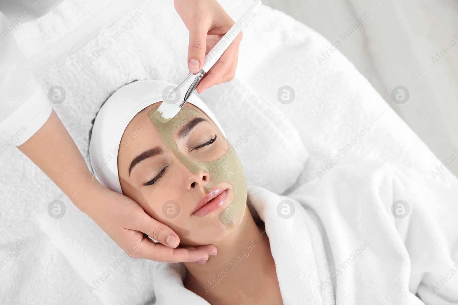 Photo of Cosmetologist applying mask on client's face in spa salon, above view