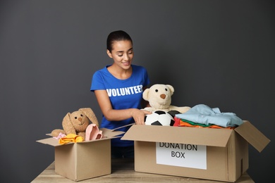 Photo of Female volunteer collecting donations at table on grey background