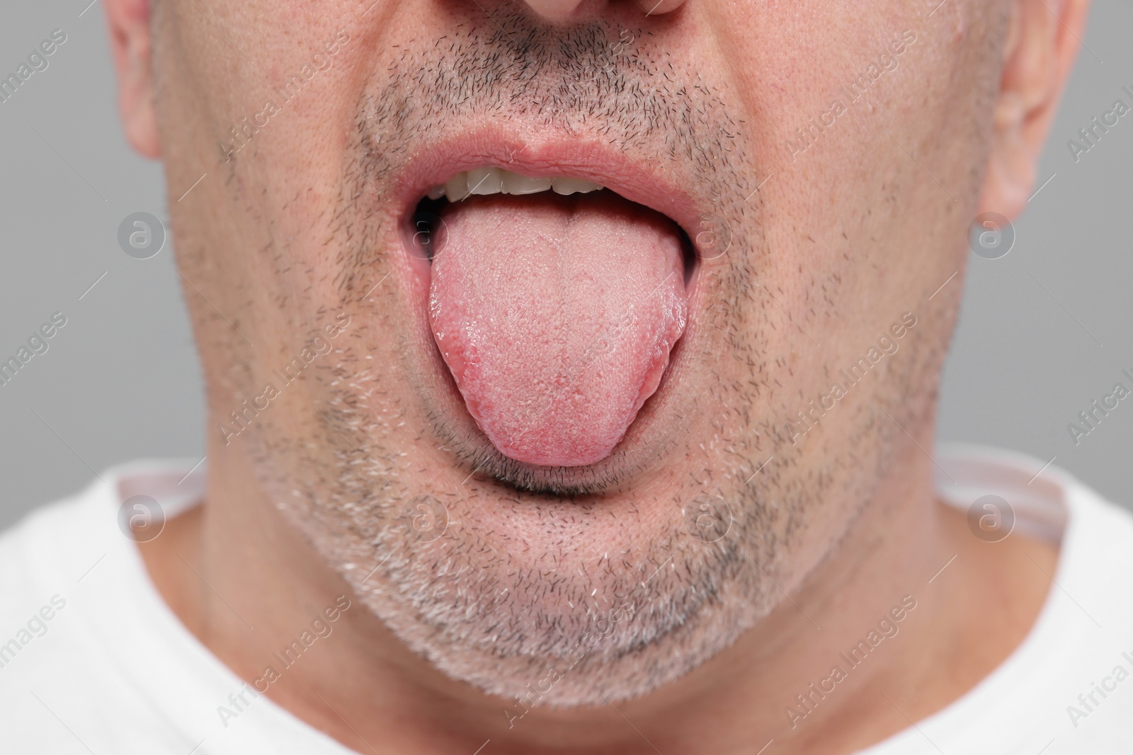 Photo of Man showing his tongue on grey background, closeup