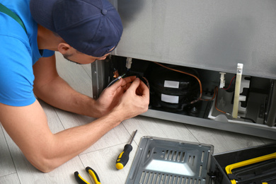 Photo of Professional male technician repairing broken refrigerator indoors