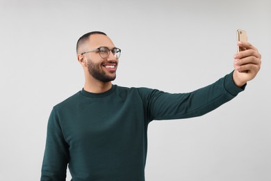 Smiling young man taking selfie with smartphone on grey background