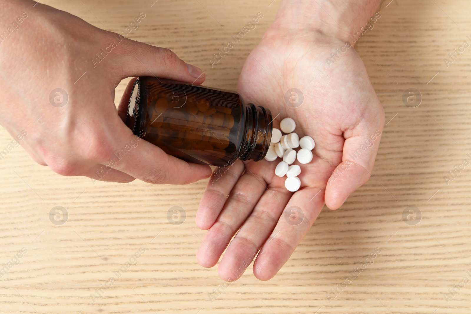 Photo of Man pouring pills from bottle at wooden table, top view