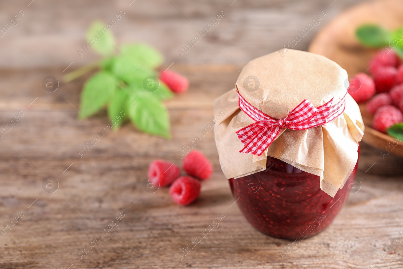 Photo of Glass jar of sweet jam with ripe raspberries on wooden table. Space for text